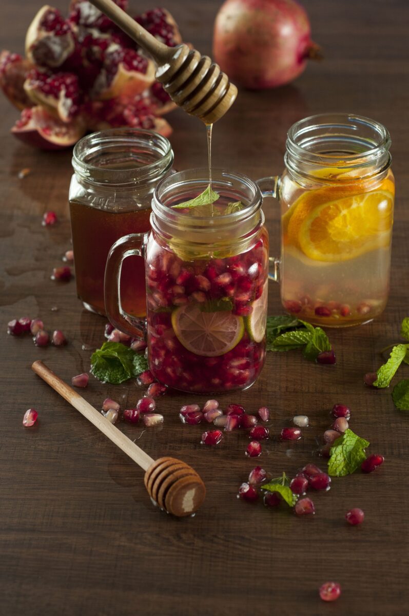 Trinkgläser mit verschiedenen Infused-Water, Honig, Granatapfelstücke und Minze dekorativ daneben