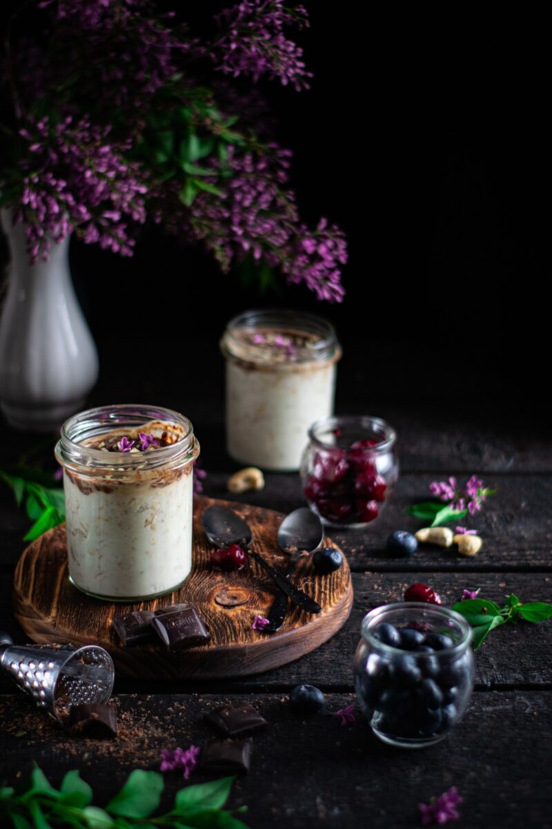 Overnight-Oats in Gläschen, dunkle Schokolade, Früchte, Nüsse und Blumendekoration außenherum